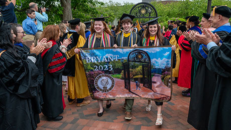Three students march with the Class of 2023 during Bryant University's undergraduate commencement exercises.