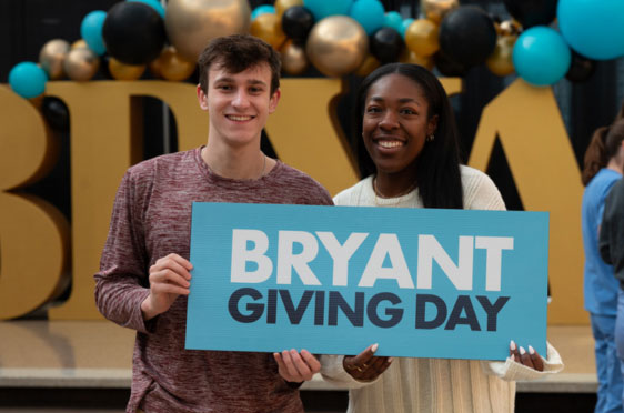 Two Bryant students hold up a Bryant Giving Day sign.